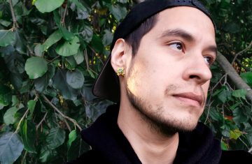 Photo of Anthony Ceballos, a young, dark-haired Native American poet; in this picture, he's standing in front of some leaves, perhaps ivy.