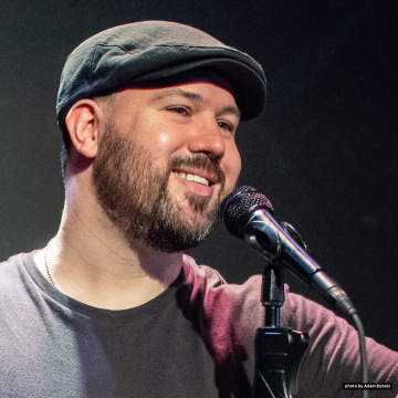 photo of Kyle Tran Myhre, also known as Guante, a light-brown-skinned man with a ruff of beard and wearing a collarless shirt and a pageboy hat. Photo by adam bubolz