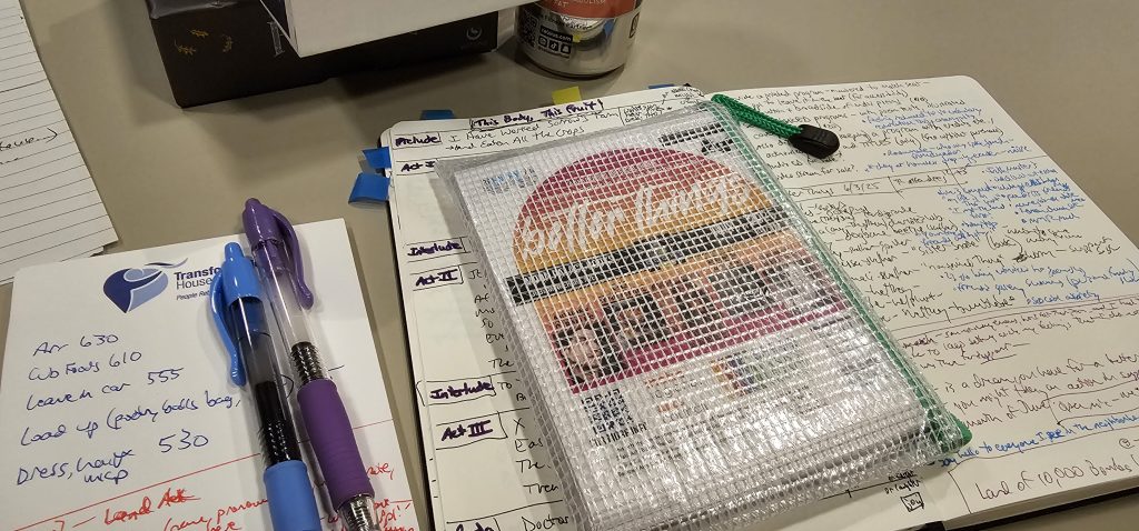 Photo from Better Things June 2025 - Davi Gray's tabletop materials, including a plastic mesh envelope with July's flyers and a notebook with some notes written in it.