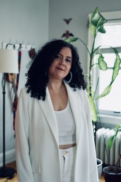 Photograph of Anaïs Deal-Márquez, a Latina woman with pale skin and long black hair, wearing a white jacket over white shirt and pants.